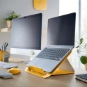 Laptop na podstawce Leitz Cosy w kolorze żółtym, obok monitor. Wszystko stoi na biurku.