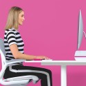 Kobieta siedzi przy biurku na różowym tle ściany, ma ergonomiczną postawę dzięki Leitz Ergo WOW.